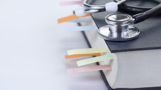 Medical student textbook with multicolor bookmarks and stethoscope, eyeglasses isolated on white with left copy-space.