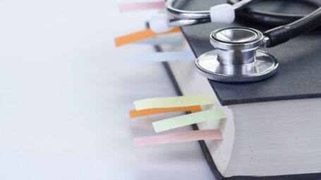 Medical student textbook with multicolor bookmarks and stethoscope, eyeglasses isolated on white with left copy-space.